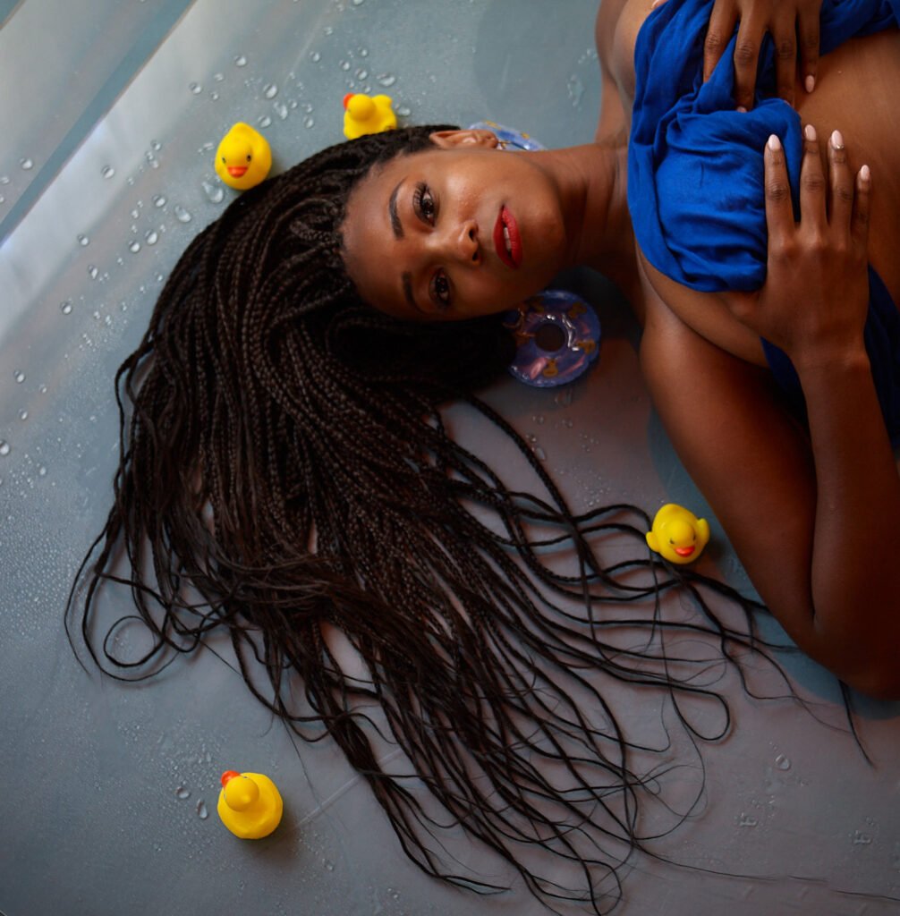 Black woman close up portrait while lying on floor with yellow rubber duckies and blue towel top.